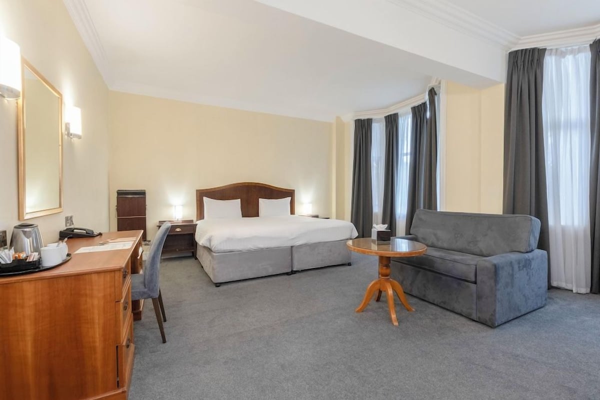 Ein Hotelzimmer mit Bett, Schreibtisch, Stuhl, Sofa und einem kleinen runden Tisch.