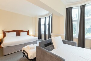 Een hotelkamer met twee bedden, een bank en een raam met gordijnen.