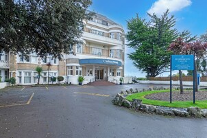 Een hotelingang met een bord voor het Carlton Hotel, een parkeerplaats en een aangelegde tuin.