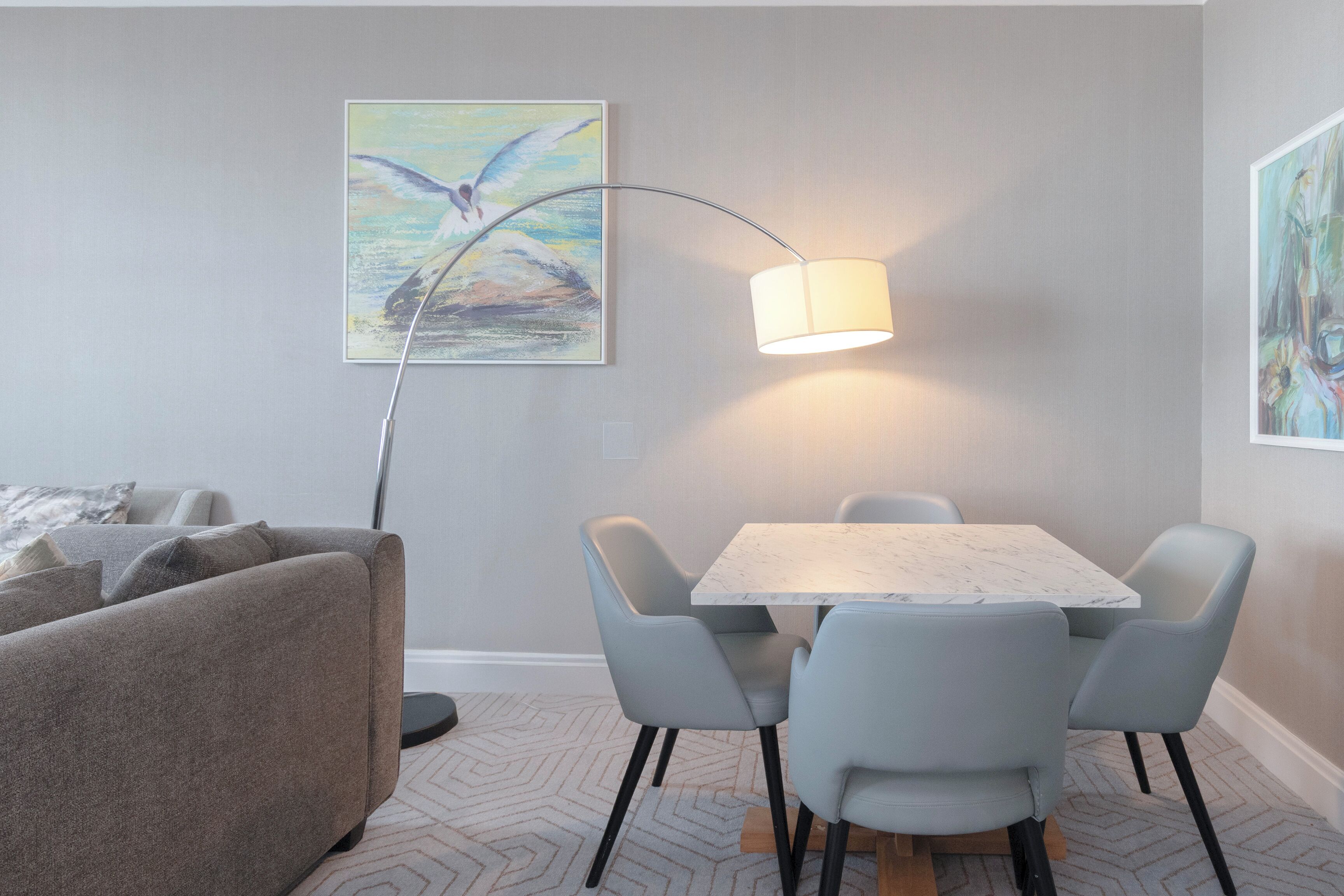 A dining area with a table and chairs, a floor lamp, and a painting on the wall.