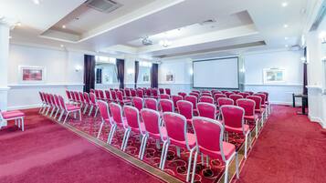 A conference room with rows of red chairs, a projector screen, and a carpeted floor.