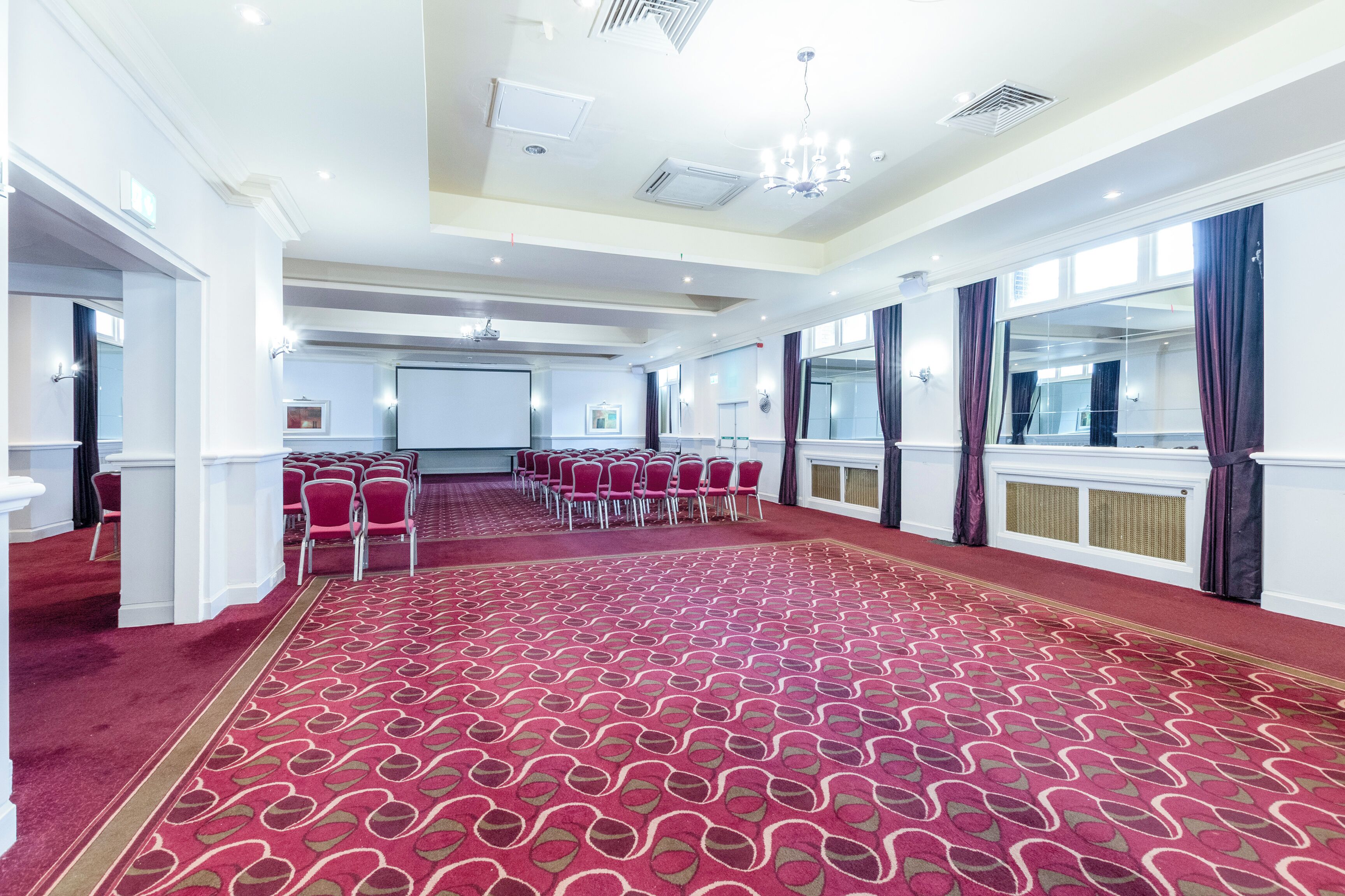 Une salle de conférence avec un tapis rouge, des murs blancs et un écran de projection.