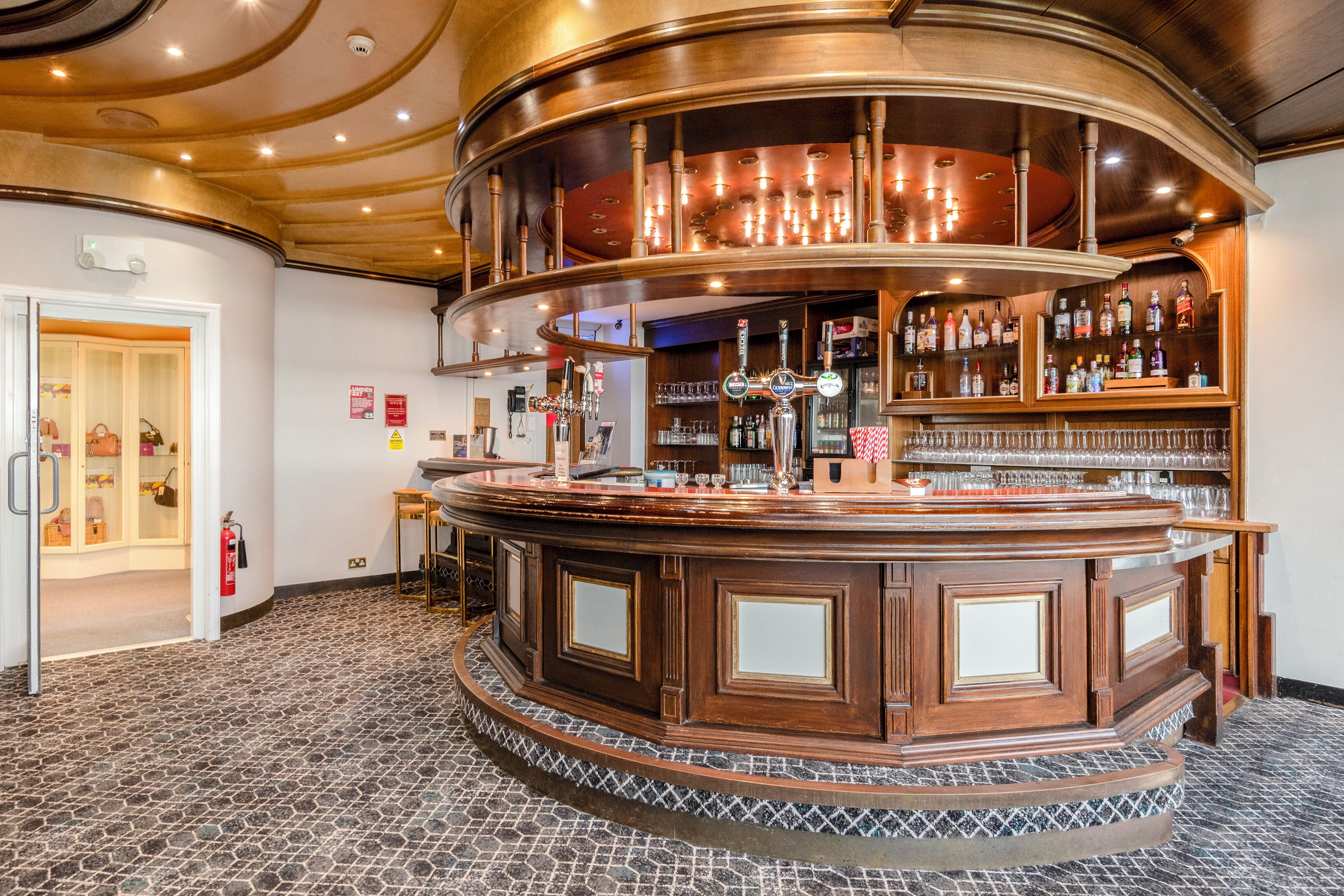 A bar area with a curved wooden counter, multiple taps, and shelves stocked with bottles.
