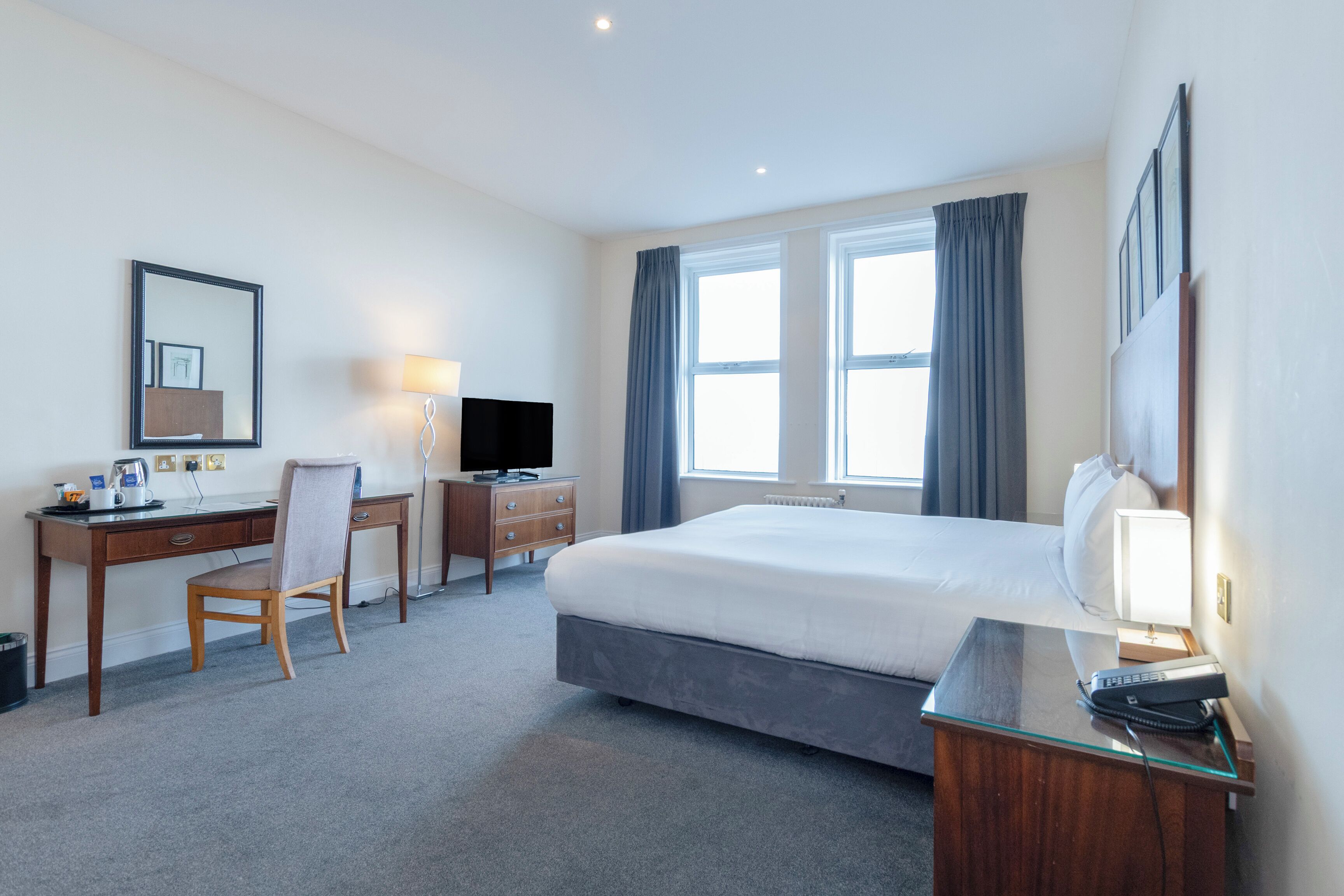 Ein Hotelzimmer mit Bett, Schreibtisch, Stuhl, Fernseher und Fenstern.