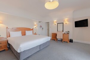 Un dormitorio con una cama grande, mesitas de noche, un aparador, un televisor montado en la pared y una puerta que da a otra habitación.