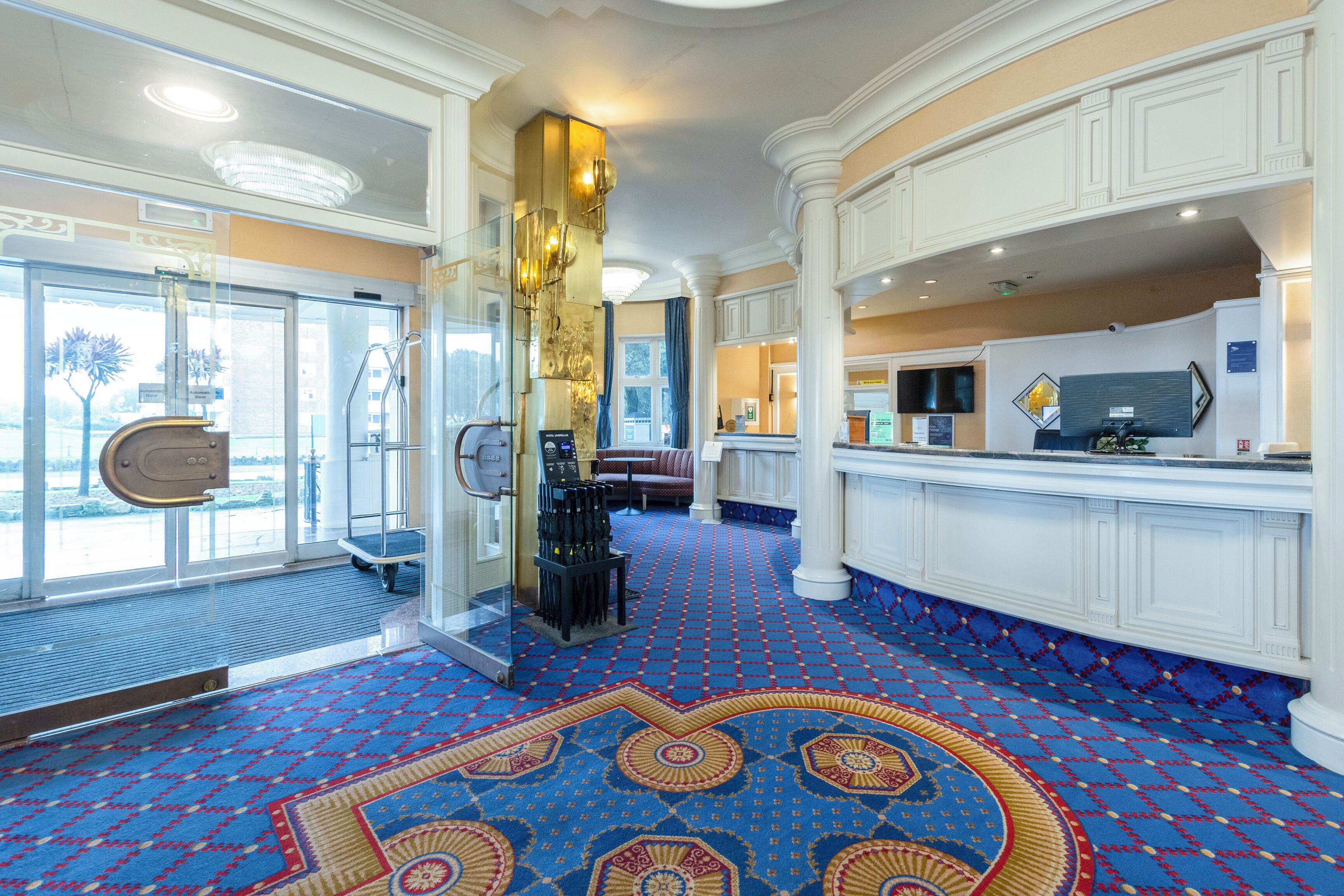 Een hotelhal met een patroon tapijt, een receptiebalie en een glazen entree.