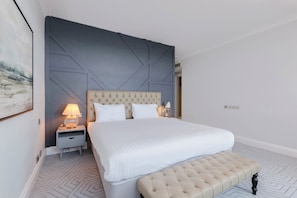 A neatly arranged hotel room with a large bed, a bedside table with a lamp, a bench, and a geometric-patterned carpet. - Bournemouth Carlton Hotel by Belvilla (Bournemouth)