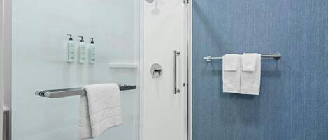 Un baño con mampara de vidrio, un perchero con dos toallas y tres botellas de champú en la pared.