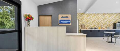 A reception desk with a 'City Express by Marriott' sign, a flower vase, and a blue doormat.