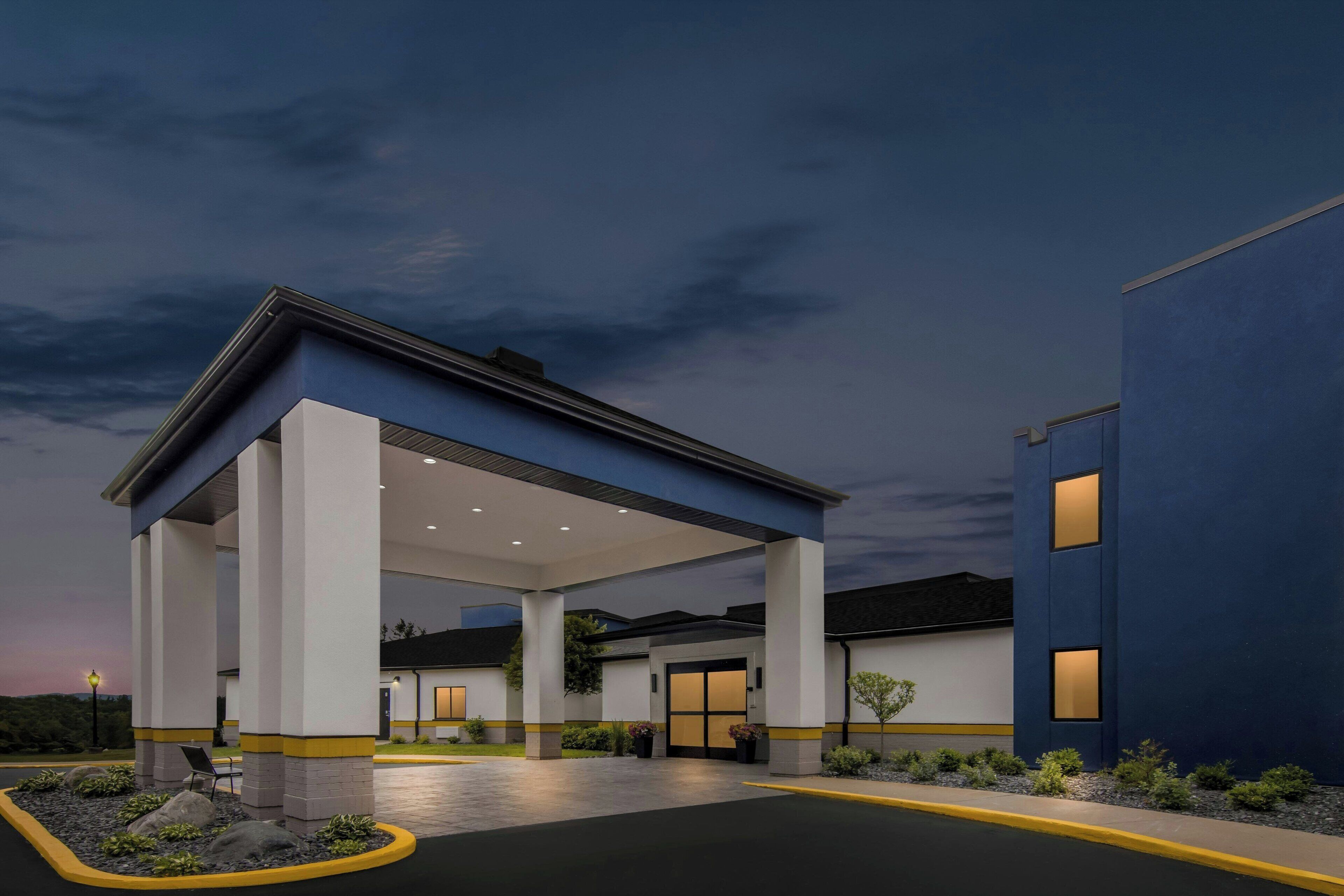 A hotel entrance with a covered waiting area, a clear sky, and a well-lit facade.