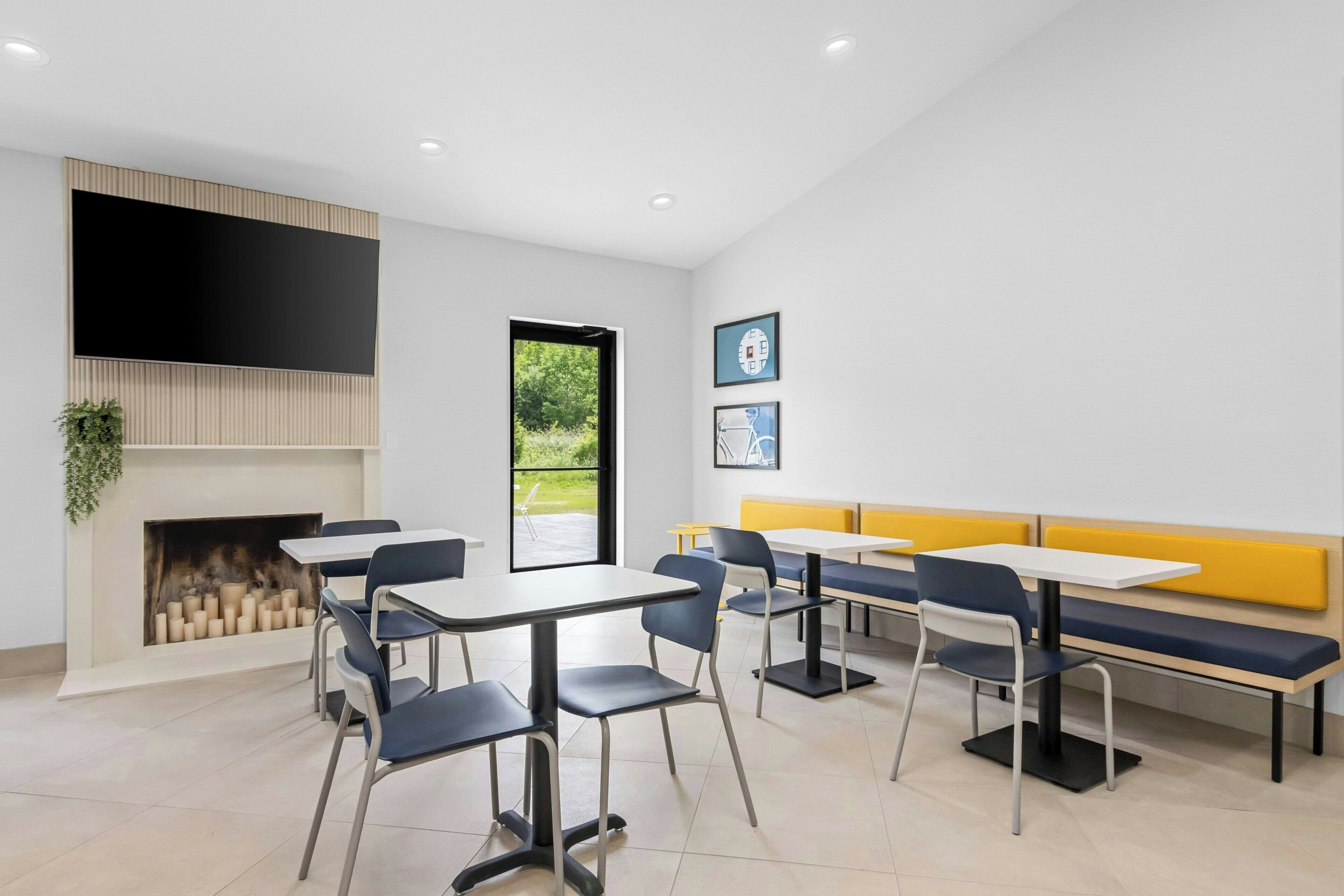 A modern dining area with tables and chairs, a fireplace, and a large window.