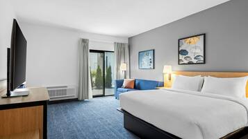 A hotel room with a bed, a desk with a TV, a sofa, and a large window.