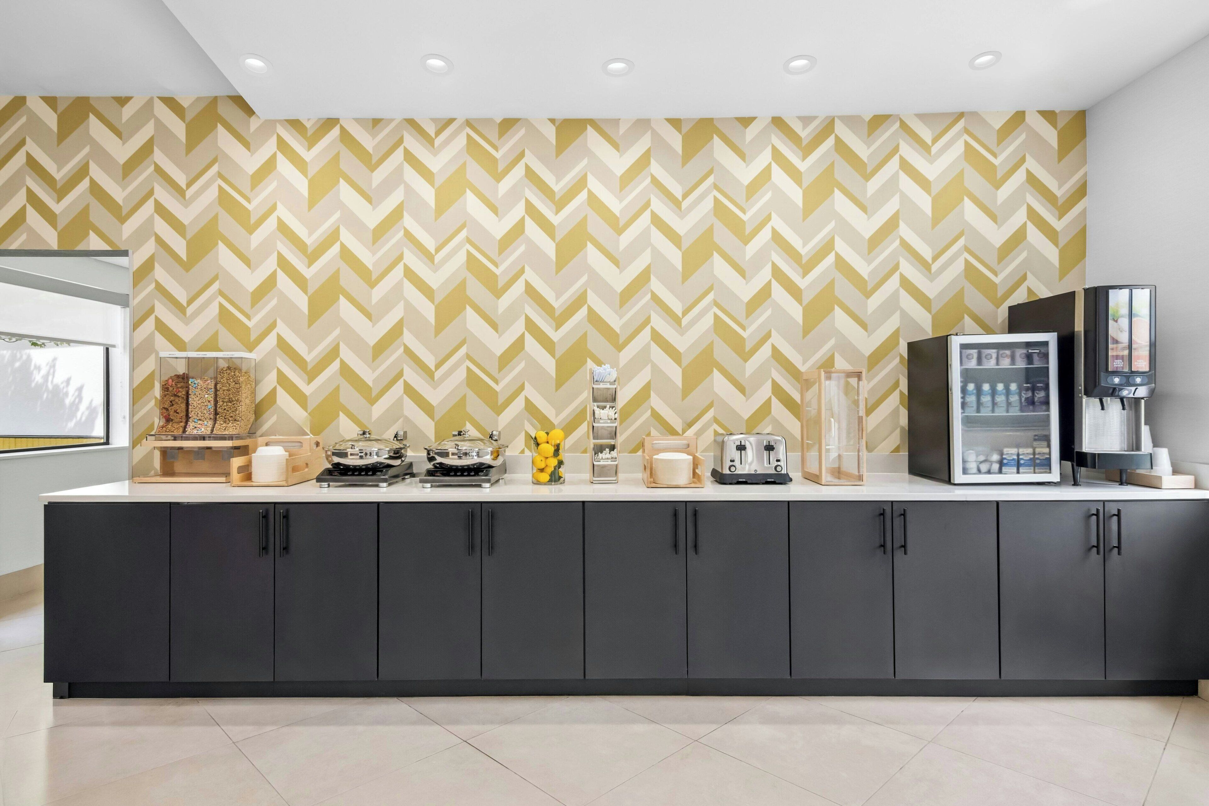 A modern kitchen with a herringbone patterned wall, a coffee station, and a refrigerator.