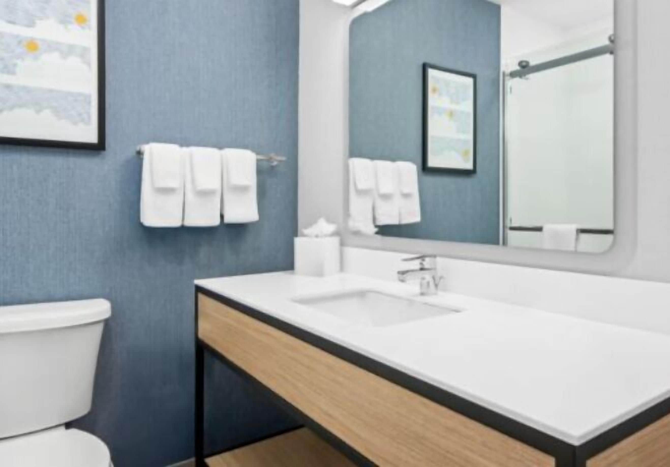 Ein modernes Badezimmer mit einem weißen Waschbecken, einem Spiegel und einer Toilette. Handtücher hängen an einem Handtuchhalter.