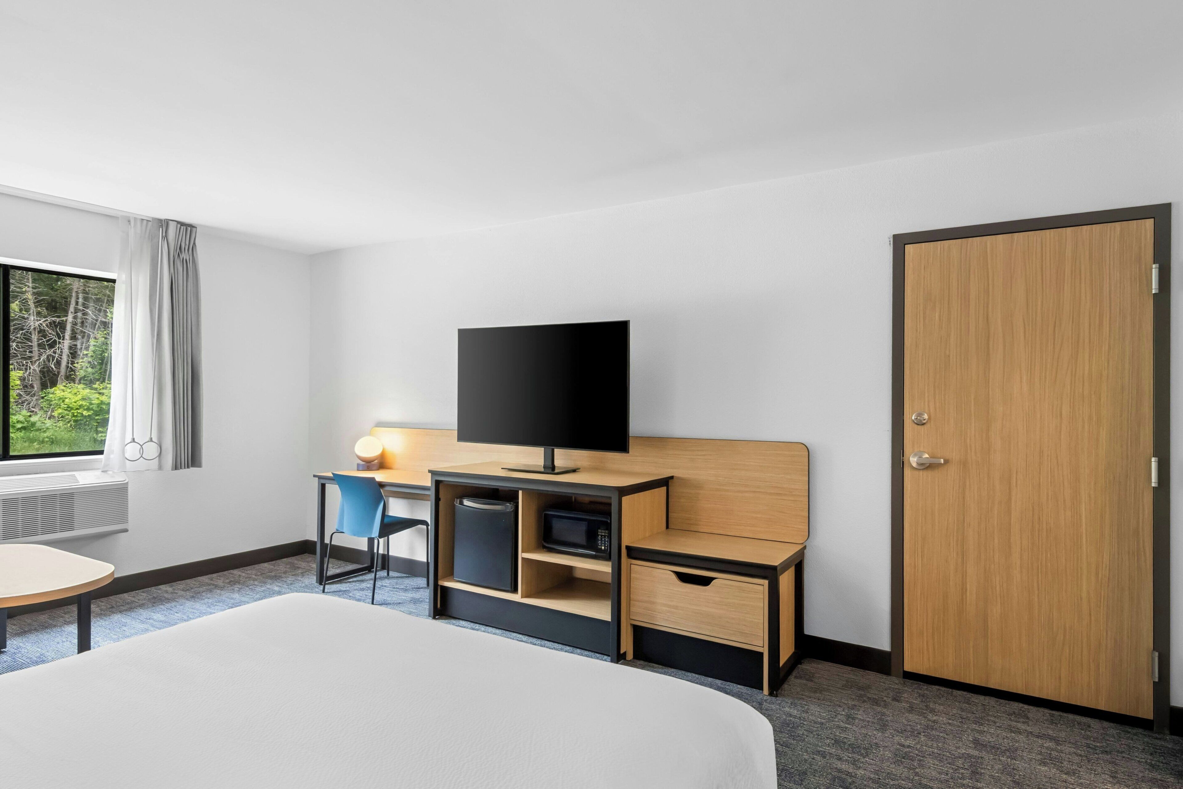 A hotel room with a bed, a desk with a computer, a television, and a wardrobe.