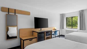 A hotel room with two beds, a desk with a flat-screen TV, a mirror, and a window with curtains.