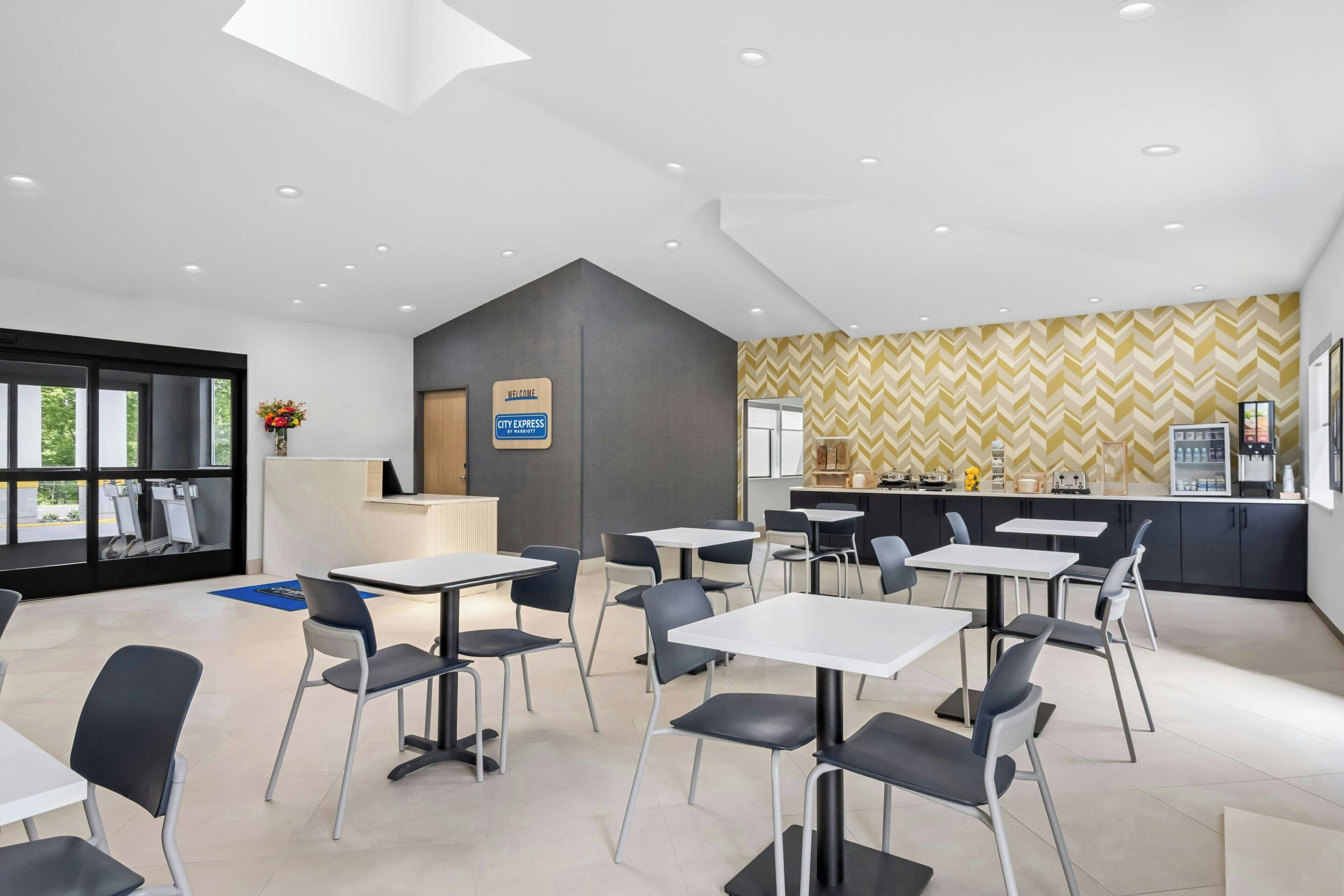 A modern cafe with tables and chairs, a reception desk, and a patterned wall.