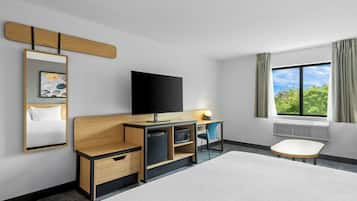 Una camera d'hotel con un letto, una scrivania con televisore a schermo piatto, una sedia, un tavolino, uno specchio e una finestra vista verde.