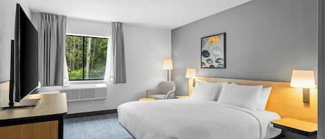 Habitación de hotel con cama, escritorio con televisor, ventana con cortinas y un cuadro en la pared.