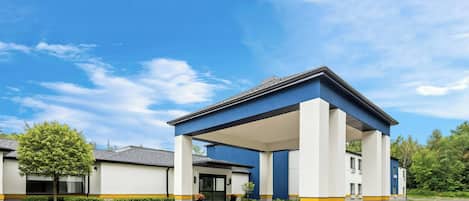 Un edificio moderno con un acceso cubierto, aparcamiento y un cielo azul despejado.