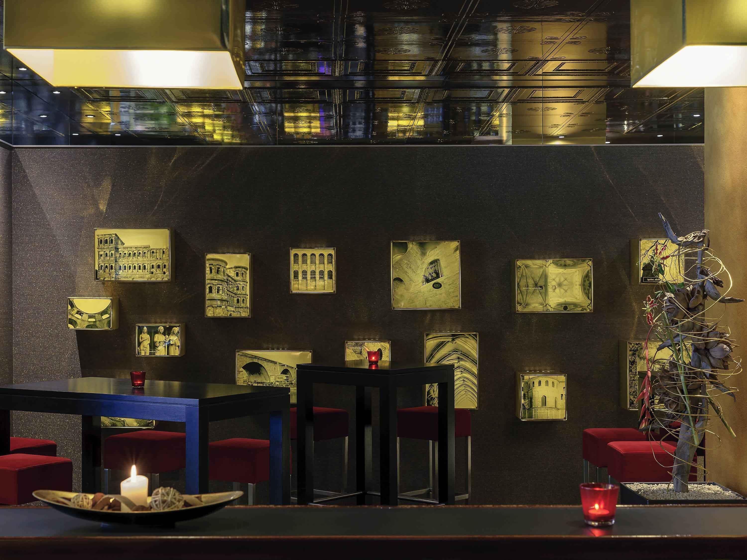 Una zona de bar con una pared oscura, varias fotos enmarcadas, sillas rojas y una planta decorativa.