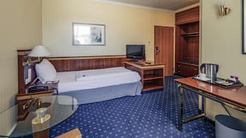 Habitación de hotel con cama, escritorio, televisor, cafetera y un pequeño cubo de basura.