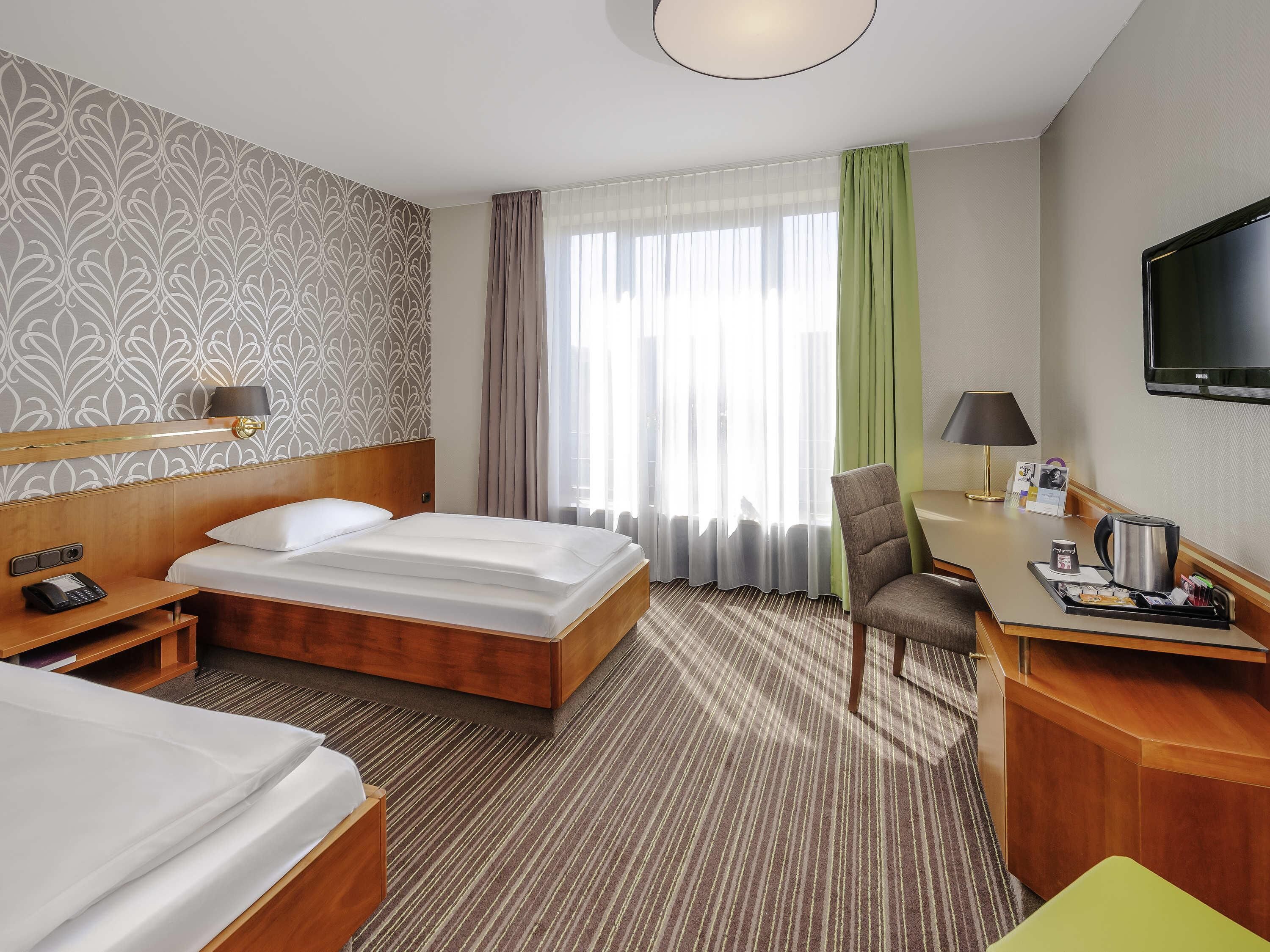 Ein Hotelzimmer mit einem Bett, einem Nachttisch mit Telefon, einem Schreibtisch mit Lampe, einem Sessel und einem Fernseher.