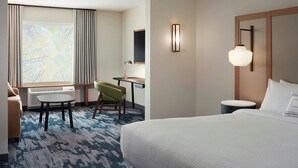 Hotelkamer met een bed, bureau, stoel, lamp en groot raam.