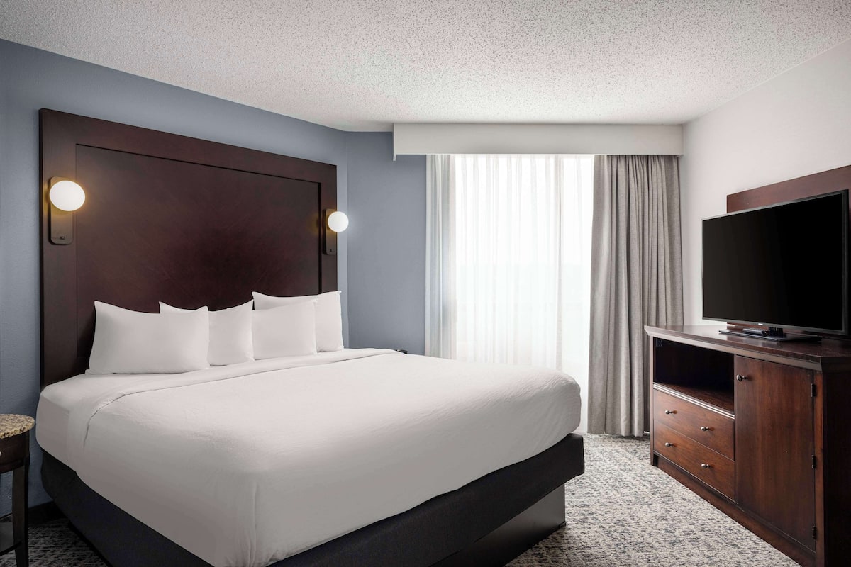 A hotel room with a large bed, a TV on a wooden cabinet, and a window with curtains.