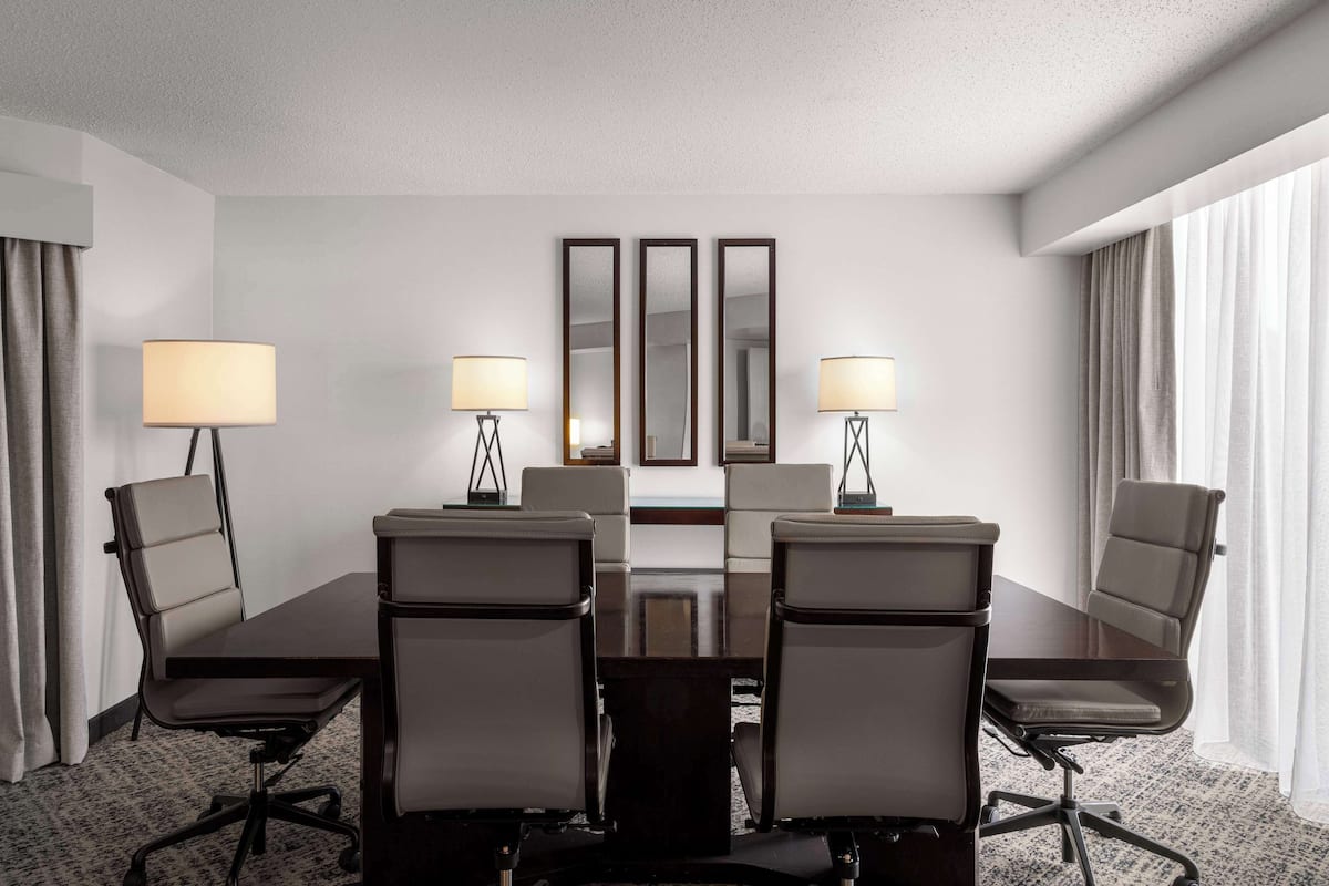 A conference room with a dark wooden table, six grey office chairs, and three wall-mounted lamps.