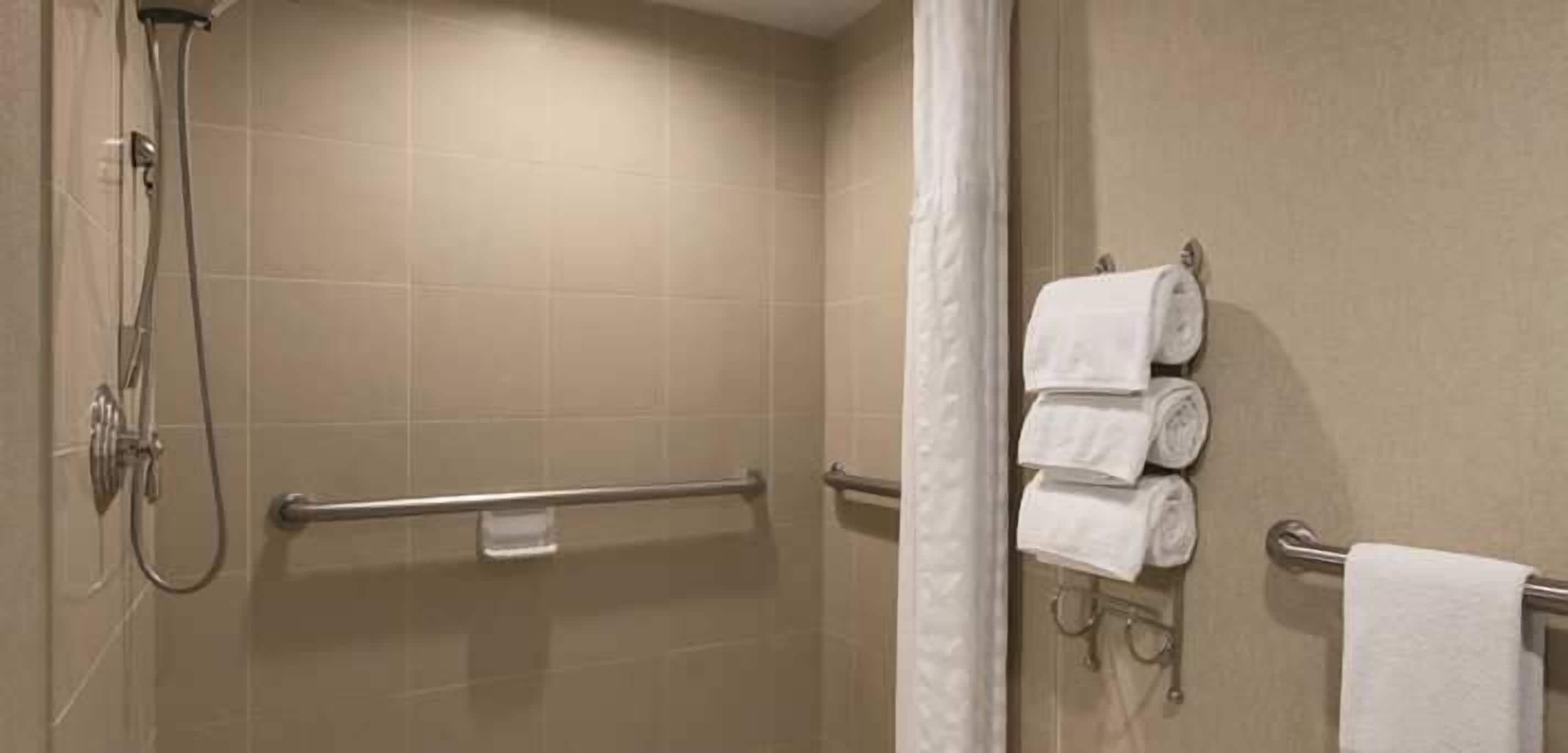 Un espace douche équipé d’une barre d’appui, d’un porte-serviettes avec des serviettes et d’un pommeau de douche.