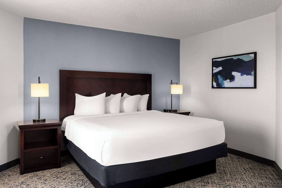 A hotel room with a large bed, two bedside tables, a headboard, and a wall-mounted abstract painting.