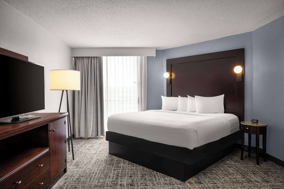 A hotel room with a large bed, a flat-screen TV, a desk, and a lamp.