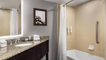 A modern bathroom with a granite countertop sink, a large mirror, a framed picture, a shower with a handheld showerhead, and a bathtub.