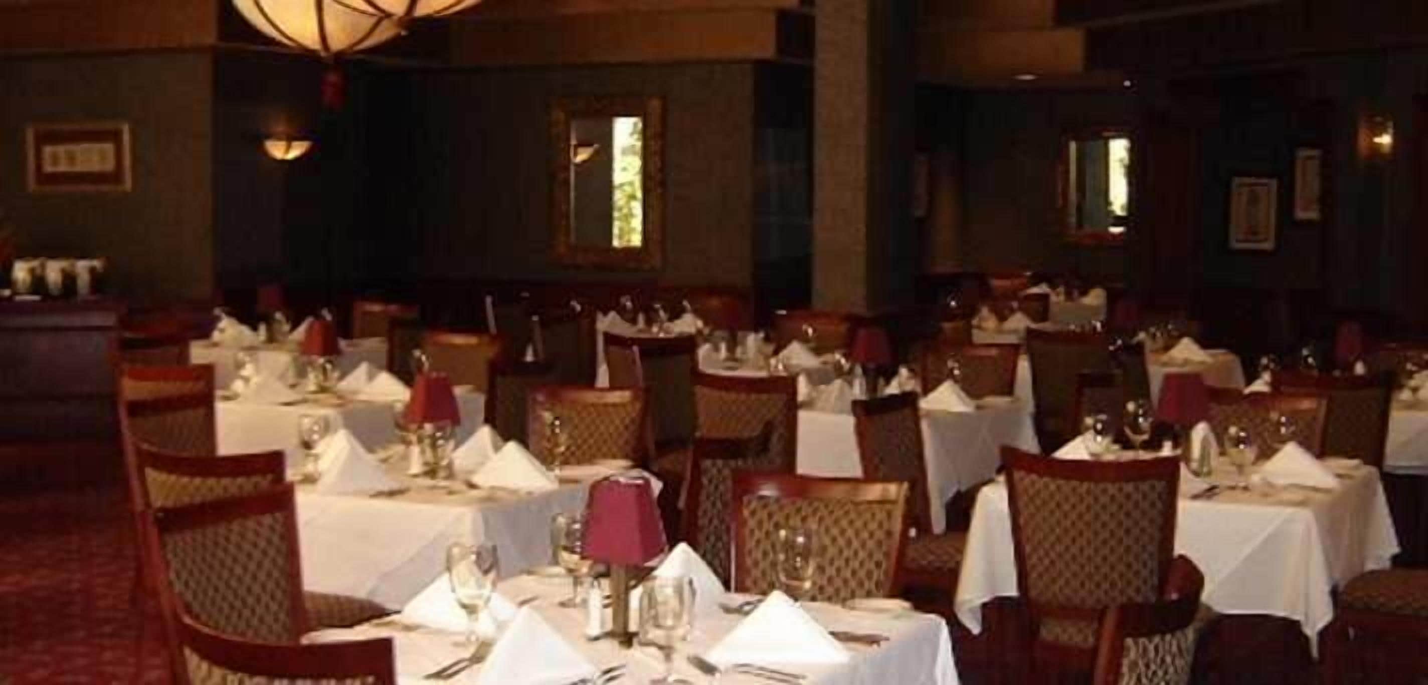 A dining area with multiple tables set for service, each with white tablecloths, red napkins, and silverware.