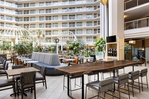 A spacious indoor atrium with multiple dining areas, seating arrangements, and a central wooden table. - Embassy Suites Hotel Birmingham (Birmingham)