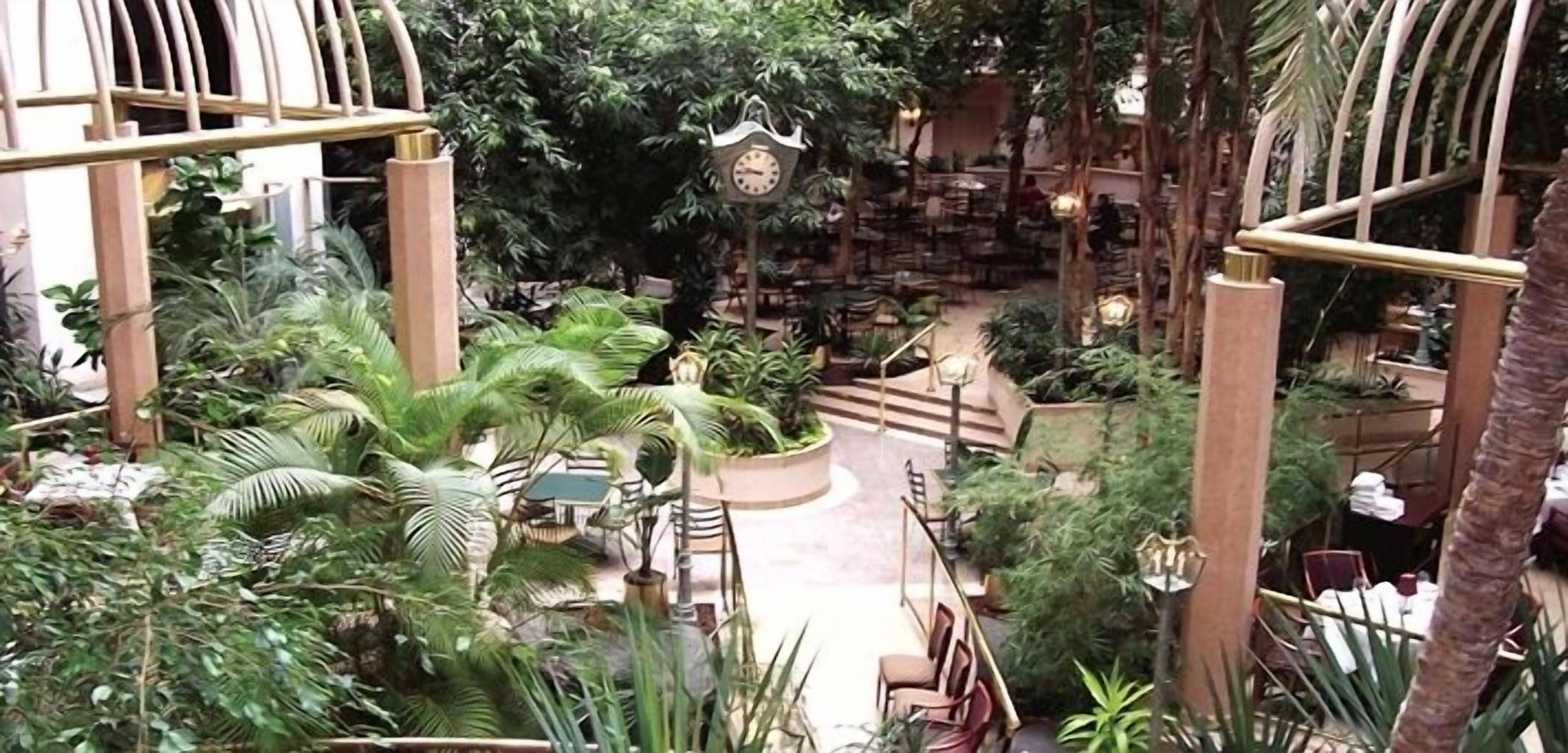An indoor atrium with a central clock, surrounded by lush greenery and seating areas.