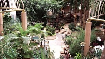 Un atrio interior con un reloj central, rodeado de exuberante follaje y zonas de estar.