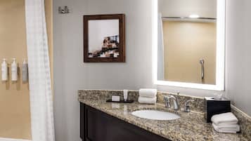 A modern bathroom with a granite countertop sink, a large mirror, and a framed picture on the wall.