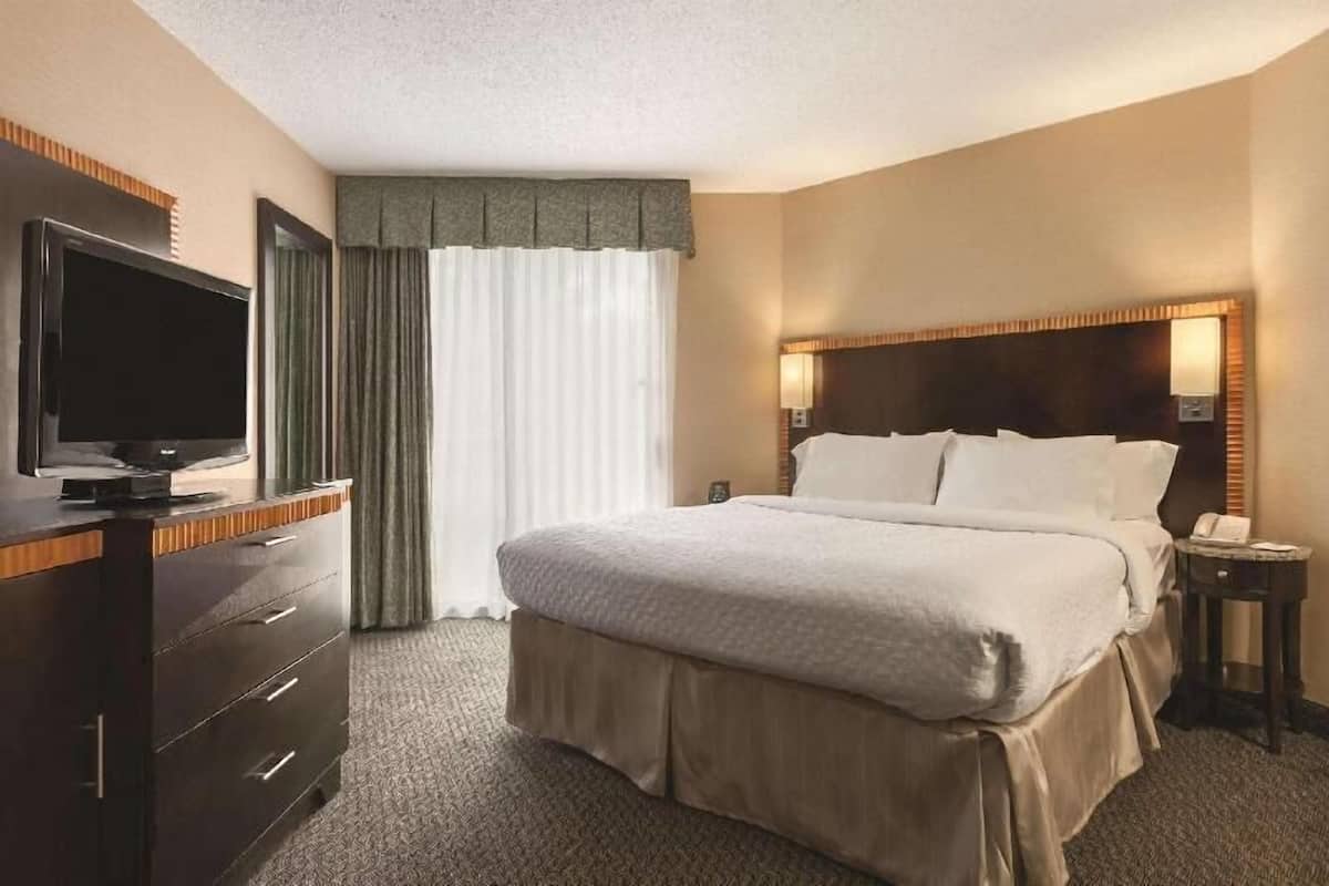 A hotel room with a bed, a TV on a dresser, a nightstand, and a window with curtains.