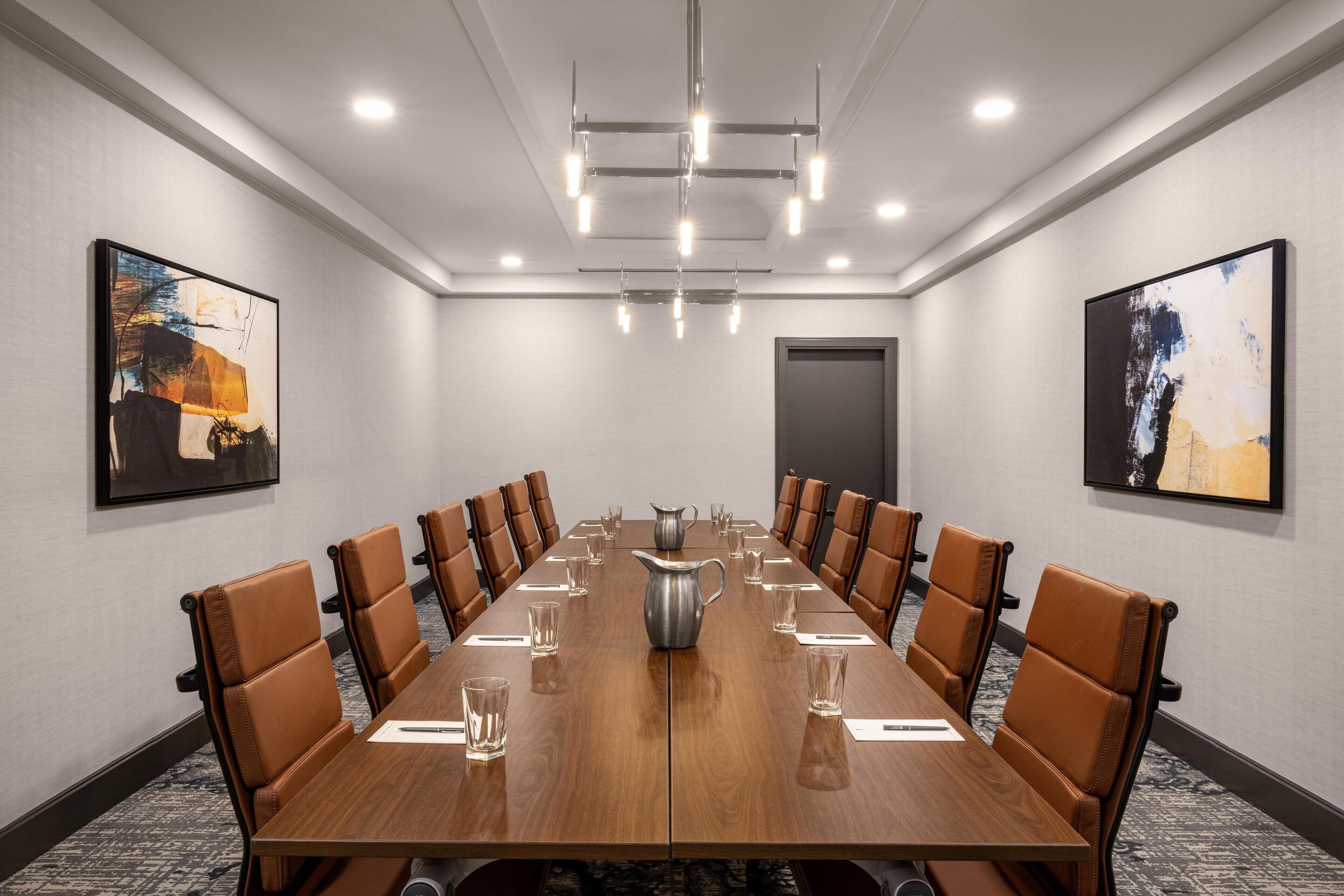 A conference room with a long wooden table, brown leather chairs, and two abstract paintings on the walls.