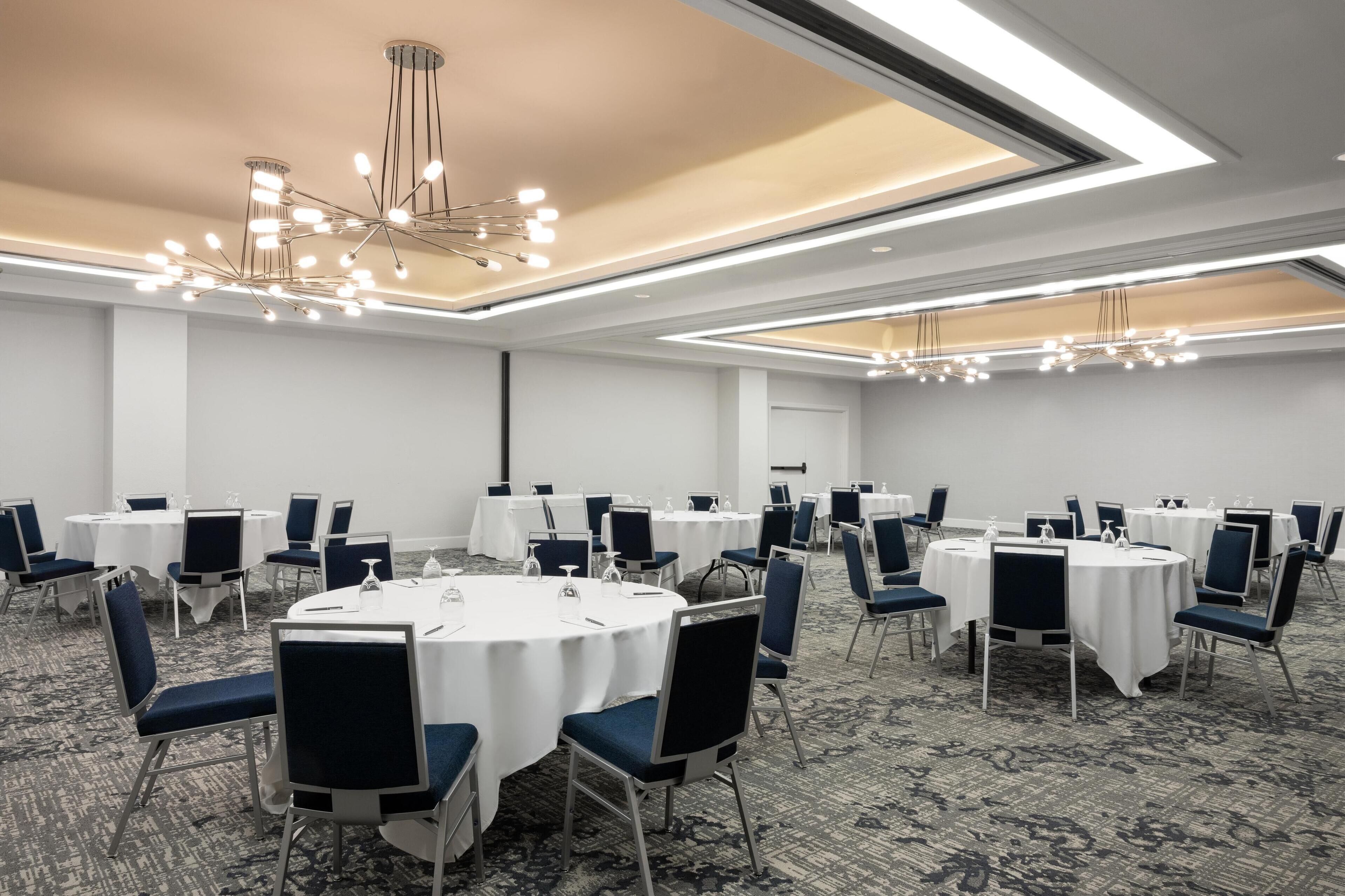 Una sala conferenze con tavoli rotondi, sedie e un lampadario moderno.