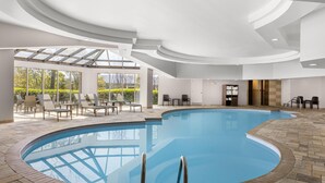 Una piscina interior de diseño curvo, rodeada de sillones de descanso y un techo de cristal.
