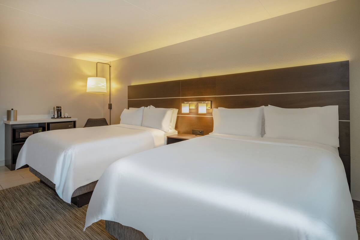 A hotel room with two beds, a desk, a lamp, and a nightstand.