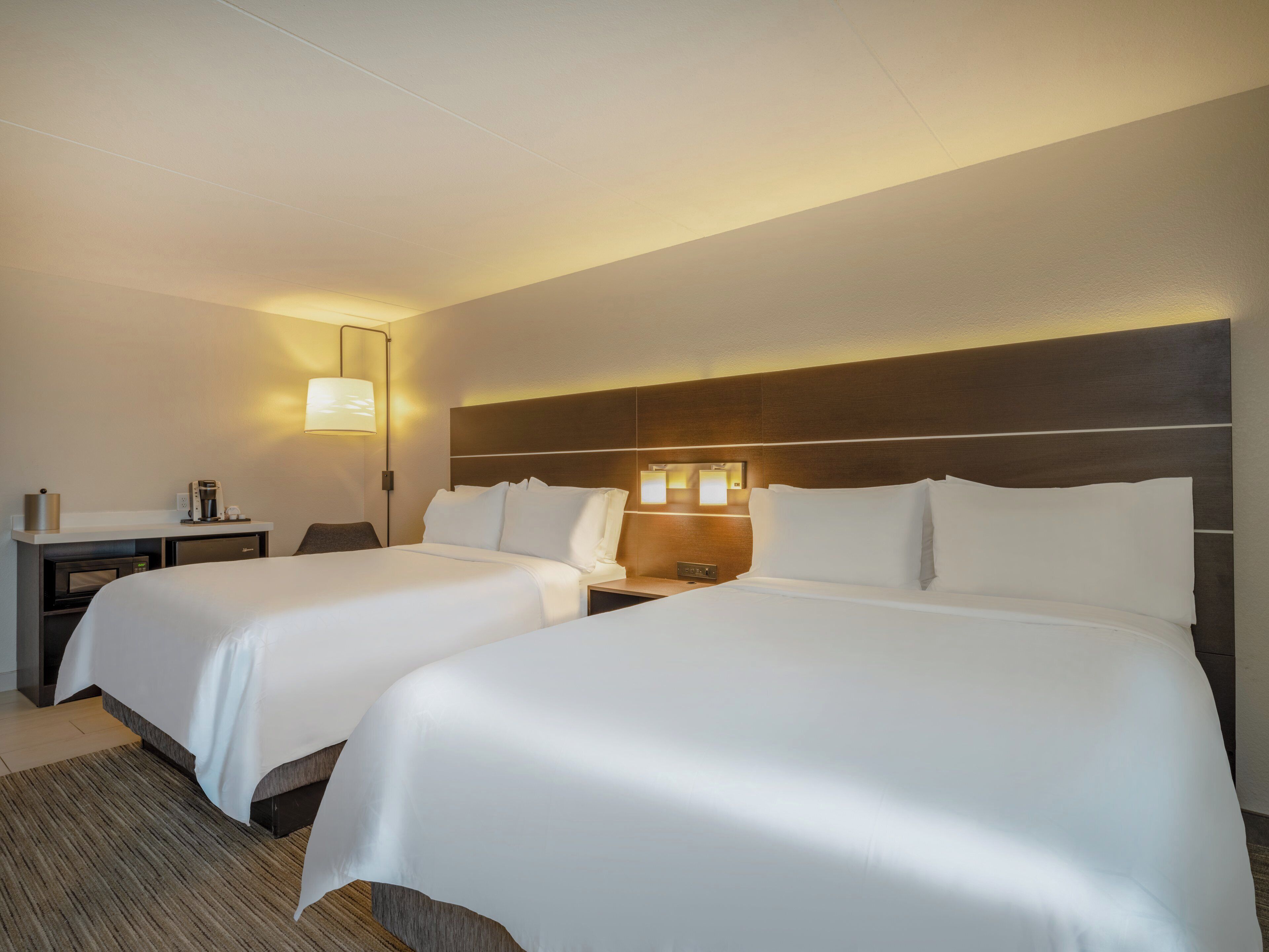 Habitación de hotel con dos camas, un escritorio, una lámpara y una mesita de noche.