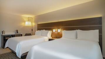 Habitación de hotel con dos camas, un escritorio, una lámpara y una mesita de noche.