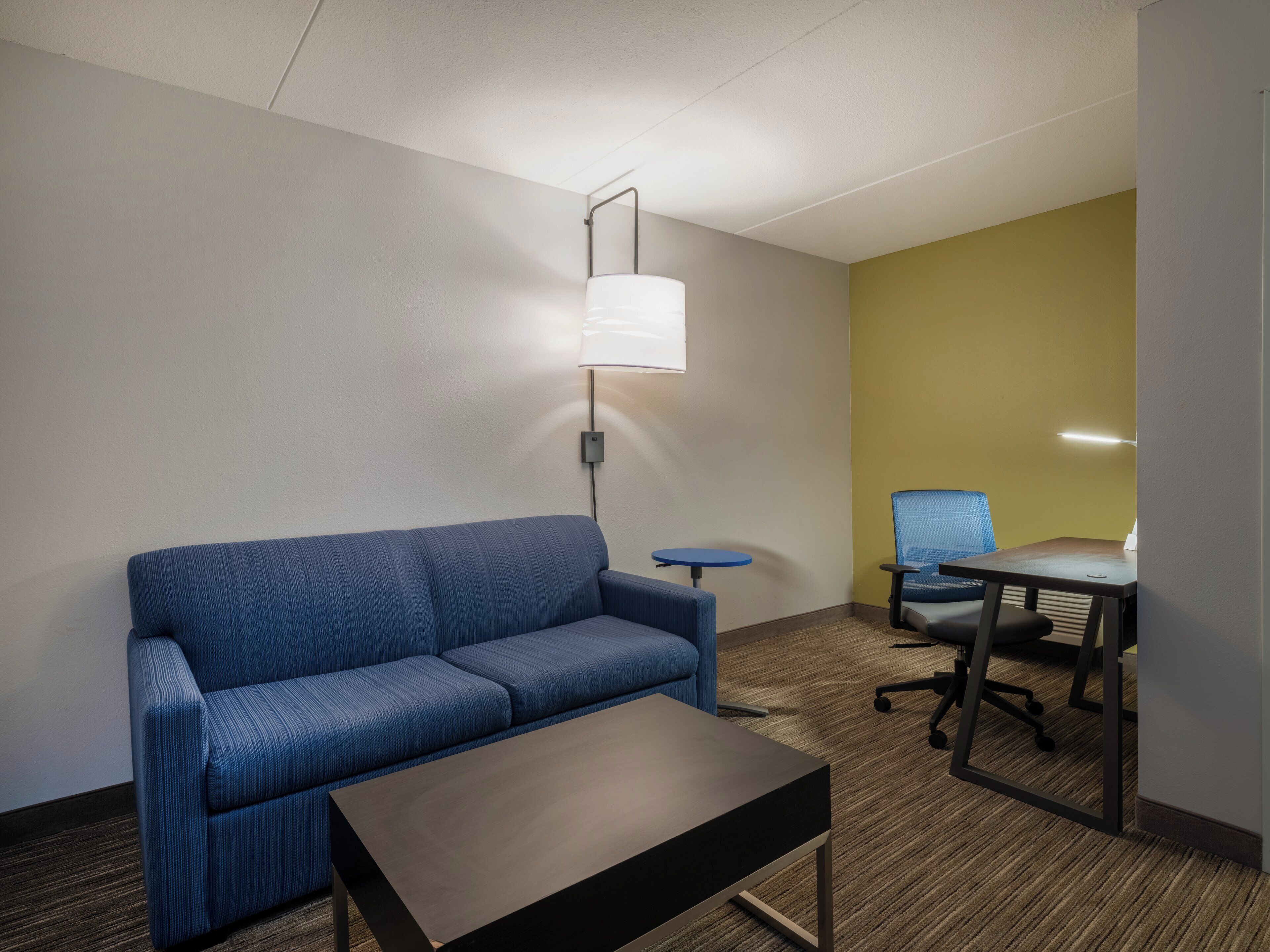 Habitación de hotel con sofá azul, una mesita, una lámpara, una silla azul y un escritorio con silla.