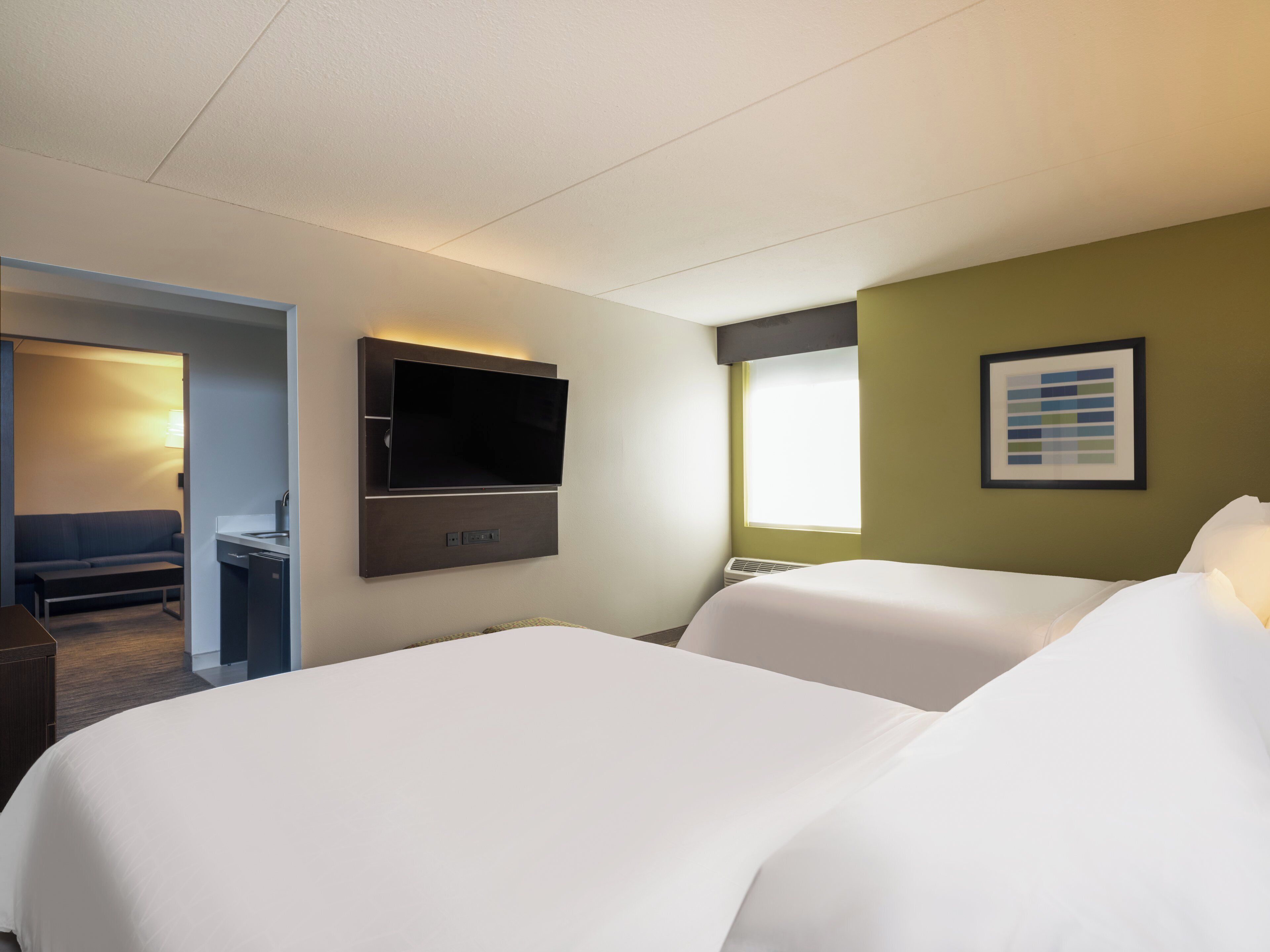 A hotel room with a bed, a TV mounted on the wall, a desk, and a window.