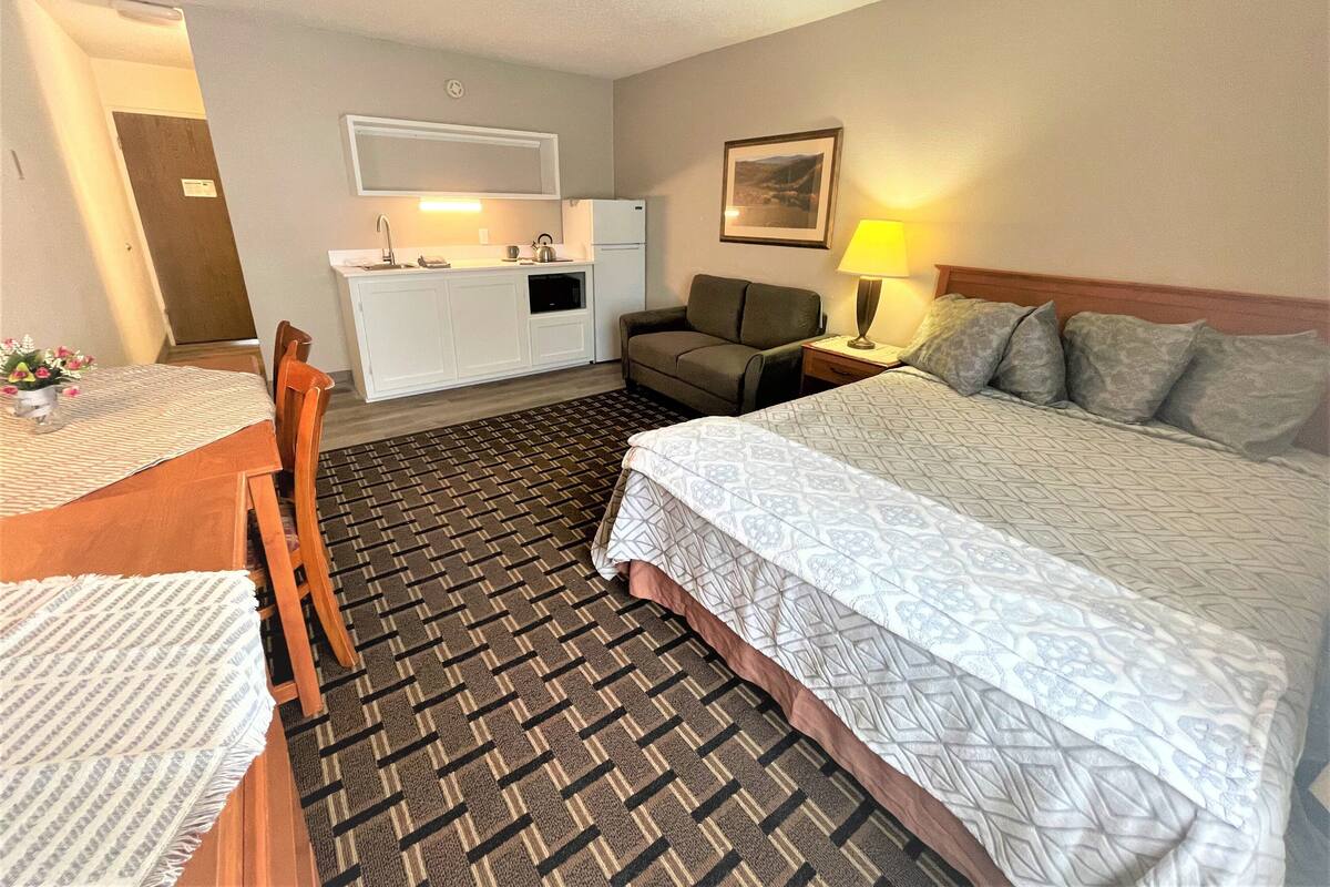 A hotel room with a bed, a sofa, a dining table, and a kitchenette.