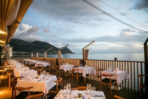 Un restaurant avec des tables dressées pour le service, offrant une vue sur un plan d’eau et une montagne.